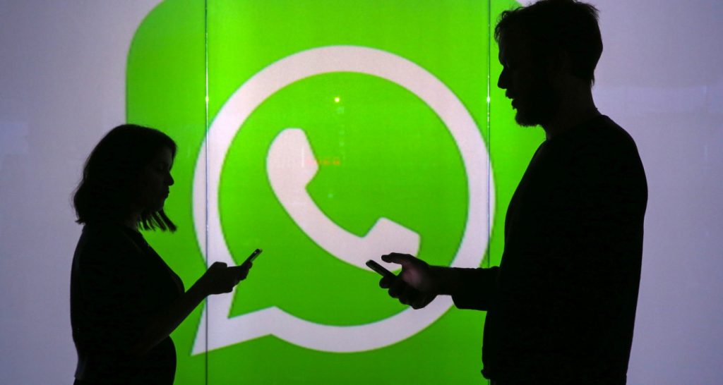 People are seen as silhouettes as they check mobile devices whilst standing against an illuminated wall bearing WhatsApp Inc's logo in this arranged photograph in London, U.K., on Tuesday, Jan. 5, 2016. WhatsApp Inc. offers a cross-platform mobile messaging application that allows users to exchange messages. Photographer: Chris Ratcliffe/Bloomberg