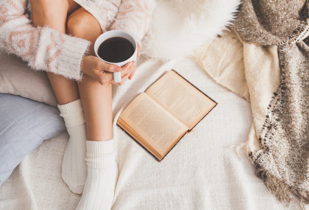 Soft photo of woman on the bed with old book and cup of coffee in hands, top view point